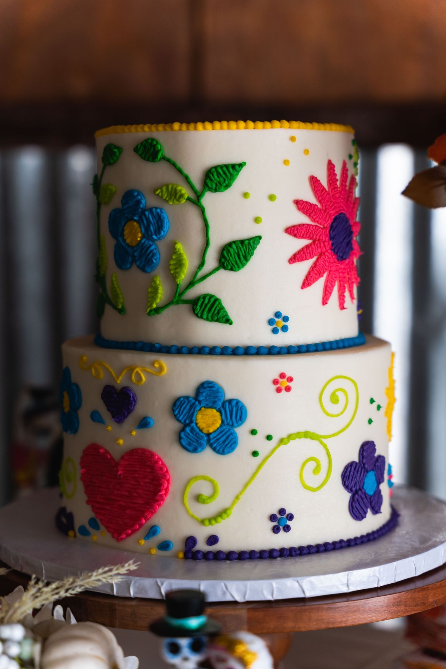 Two-tiered white wedding cake decorated with colorful floral designs and swirls.