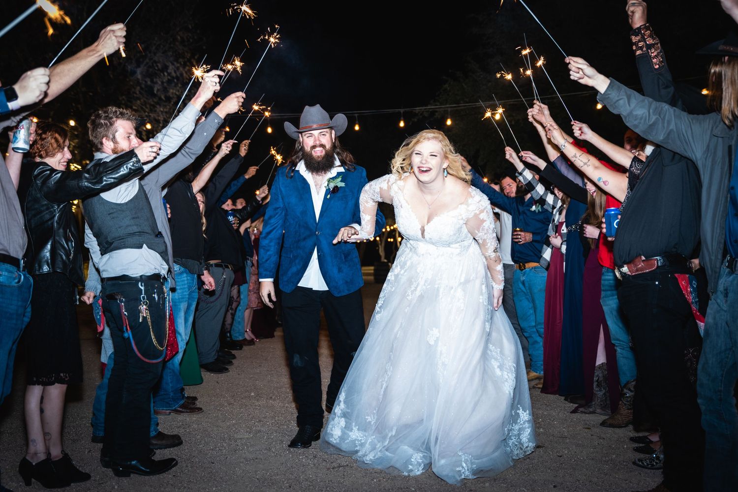 Wedding couple exits through a sparkler tunnel formed by guests during nighttime celebration.