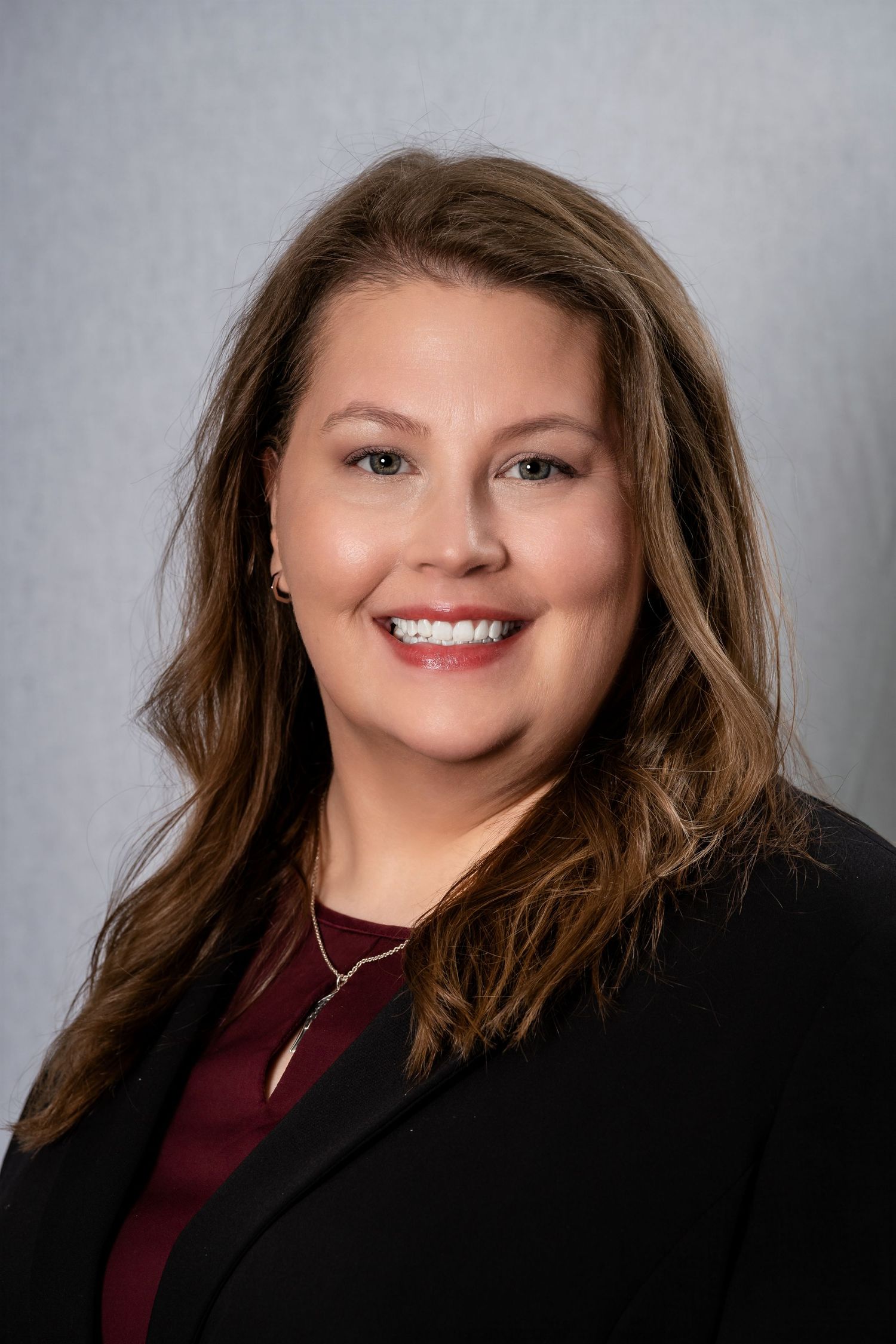 Business headshot of person in dark blazer and maroon top with warm smile.