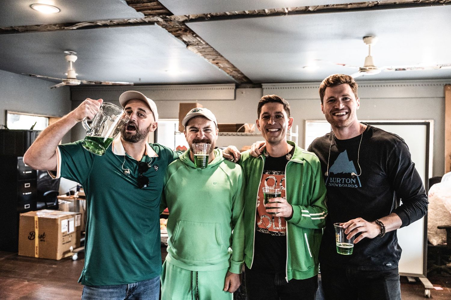 Four friends in green attire celebrating with drinks at indoor gathering.