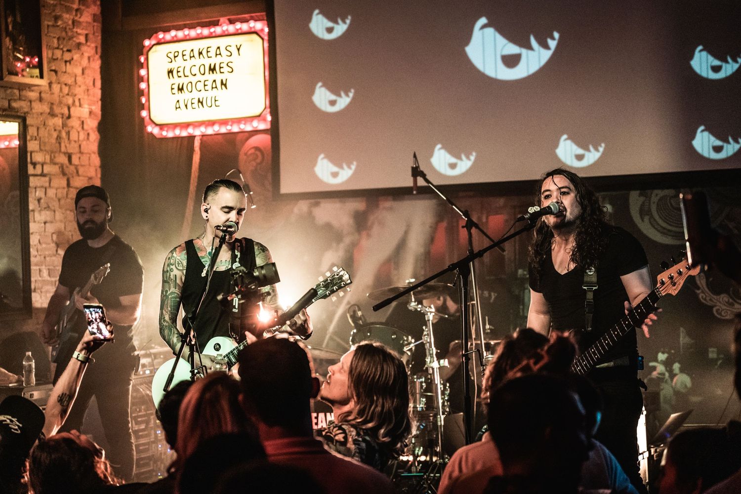 Band playing live music under vintage marquee sign with Twitter bird projections.