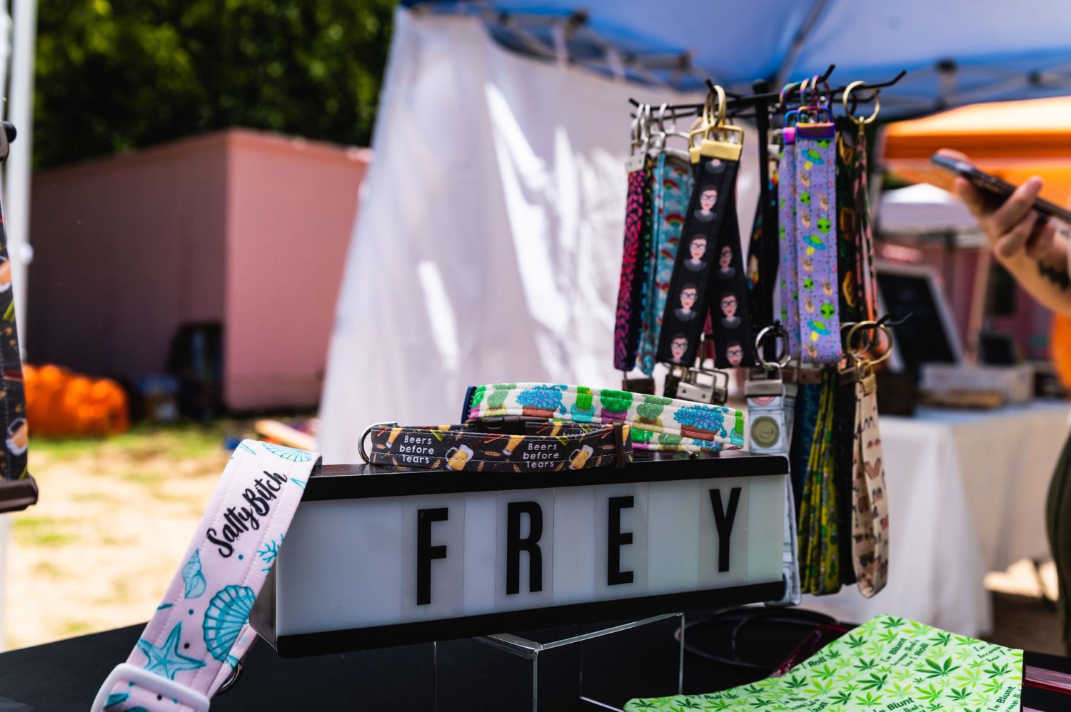 Vendor display with FREY sign and hanging accessories at outdoor market.