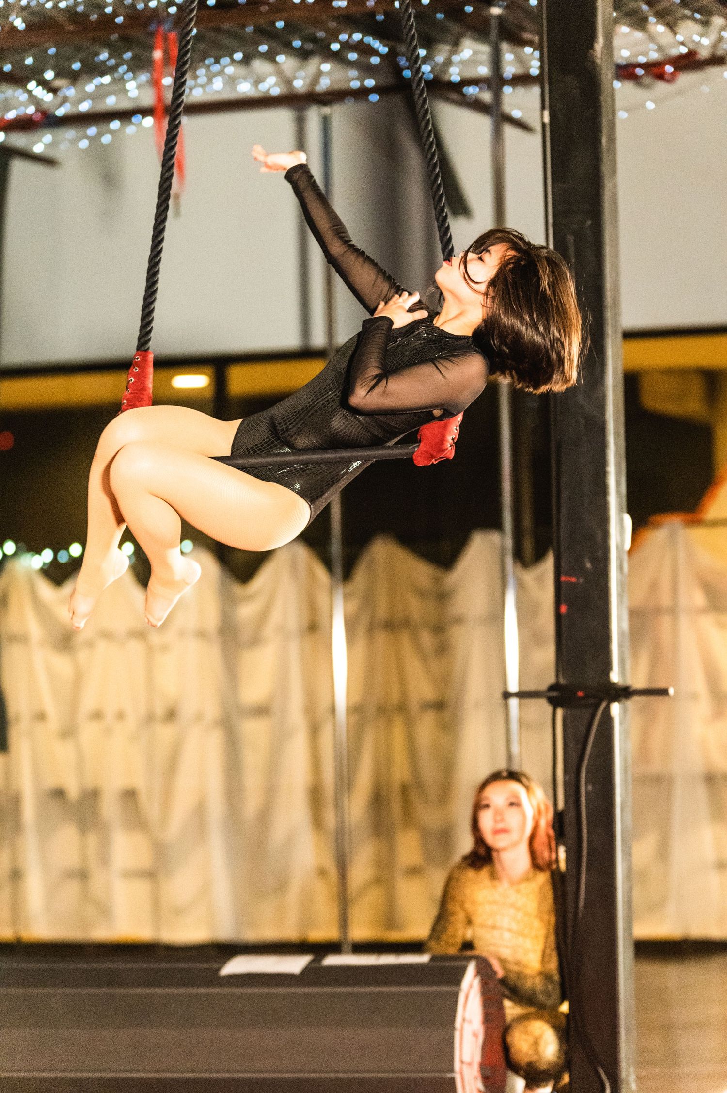 Aerial dancer performing a dynamic move on suspended equipment in a studio setting.