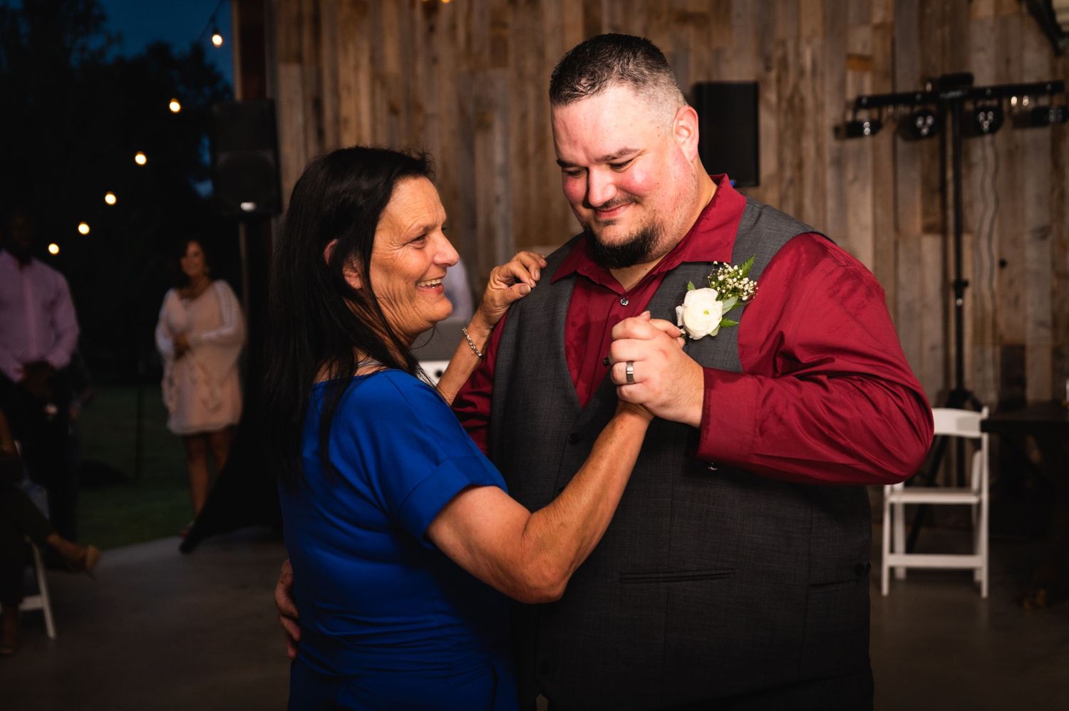 Wedding guests dance together at a rustic barn reception venue with string lights.