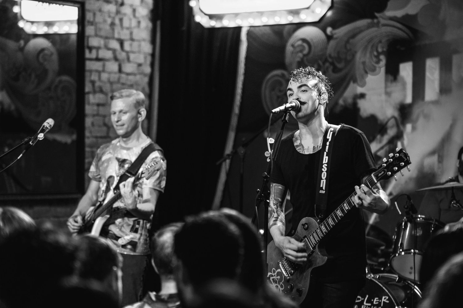 Black and white shot of performers playing guitar and singing on stage.