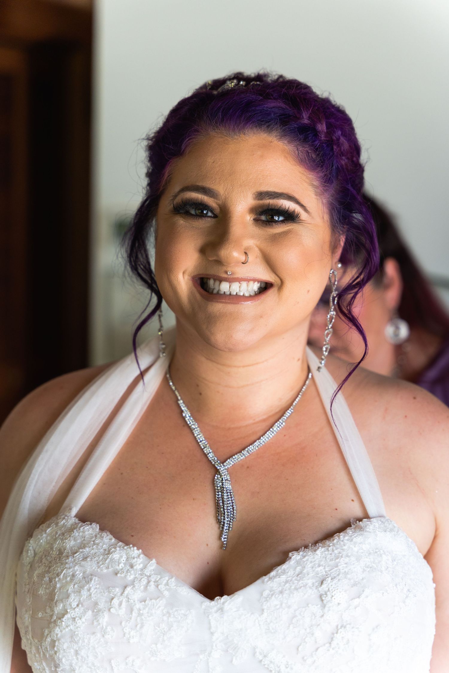 Bride with vibrant purple hair wearing a white wedding dress and crystal necklace.