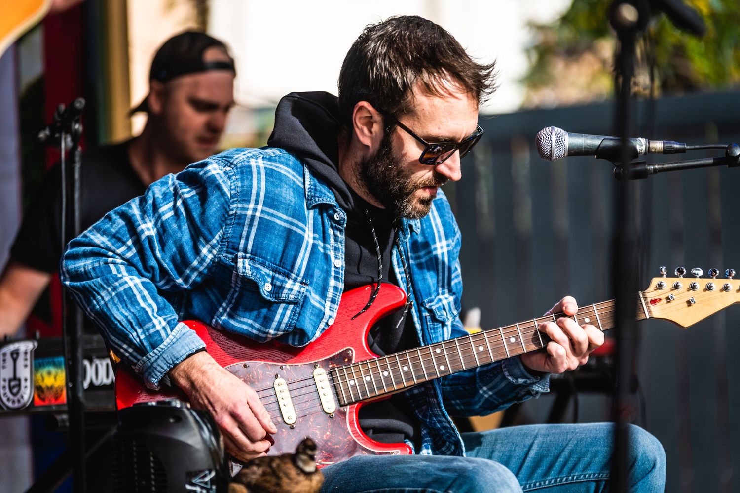Guitarist plays electric guitar during outdoor performance with sound equipment visible.
