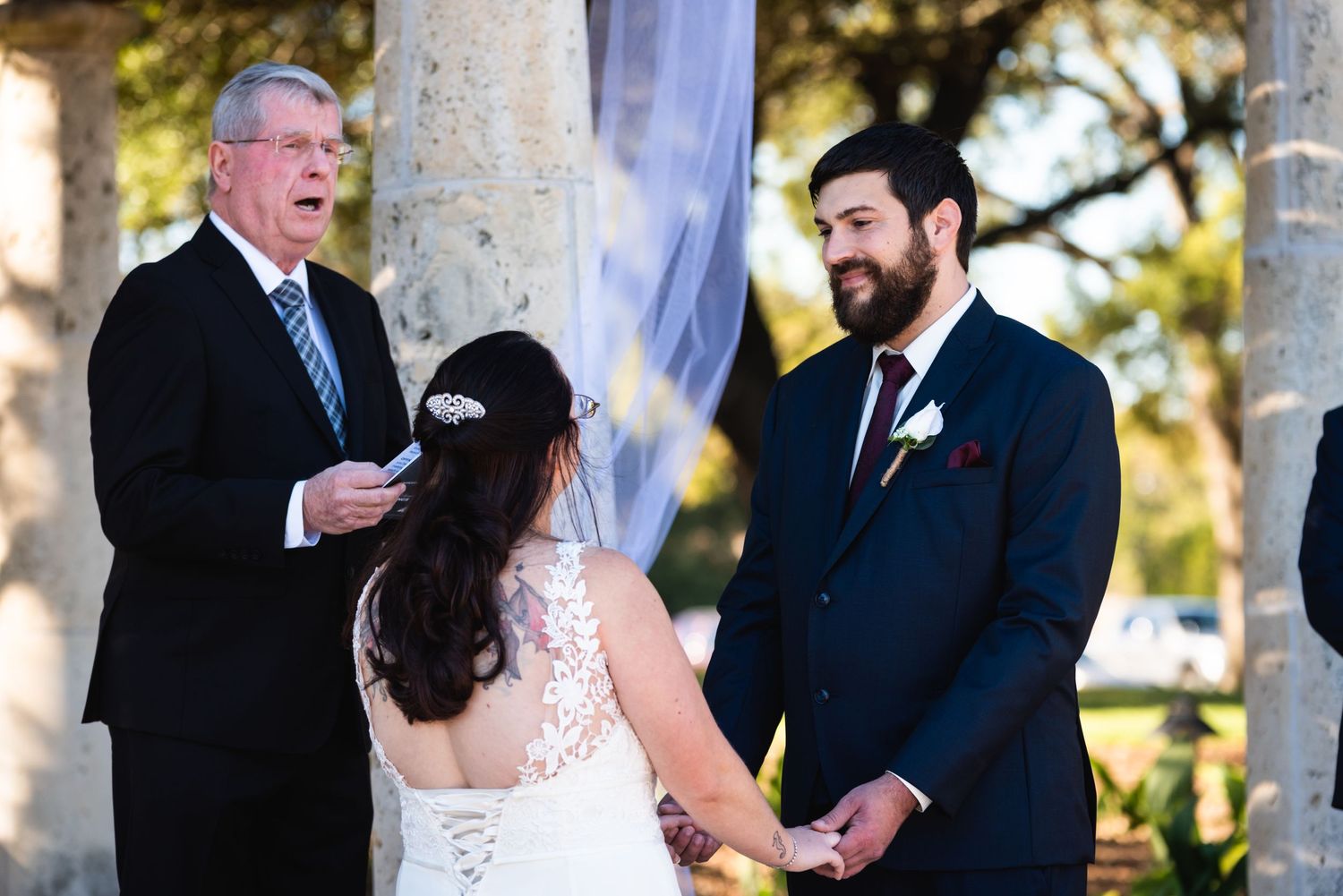 Wedding ceremony in progress with couple and officiant under elegant white pillars.