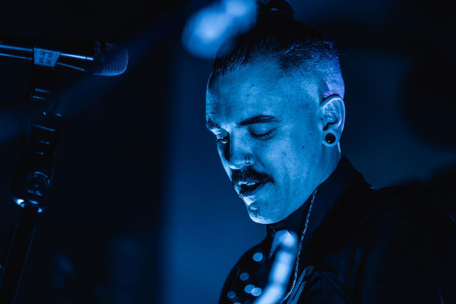 Performer illuminated in blue stage lighting sing into microphone during emotional performance.