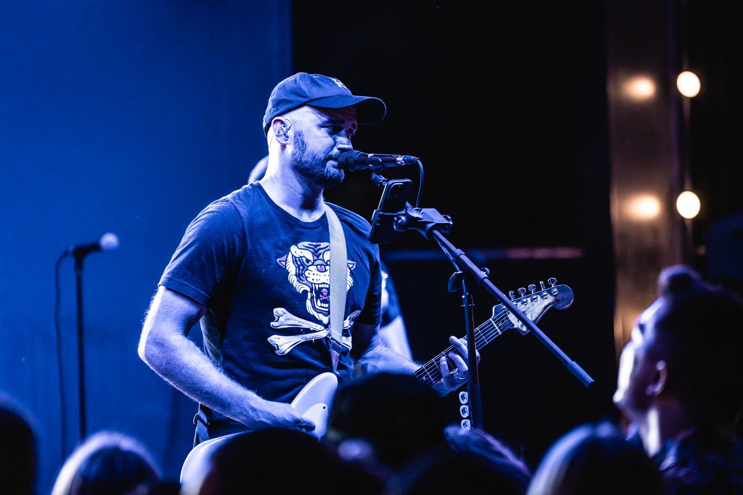 Guitar player in baseball cap performing under blue stage lights at concert venue.