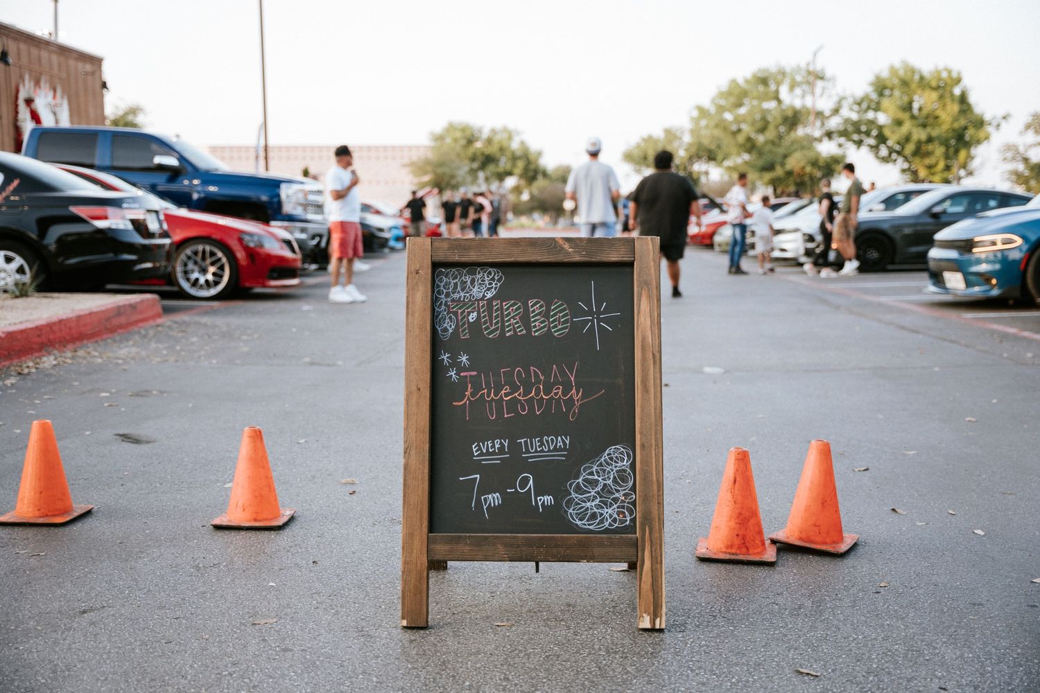 Wooden chalkboard sign with orange traffic cones at car meet event.