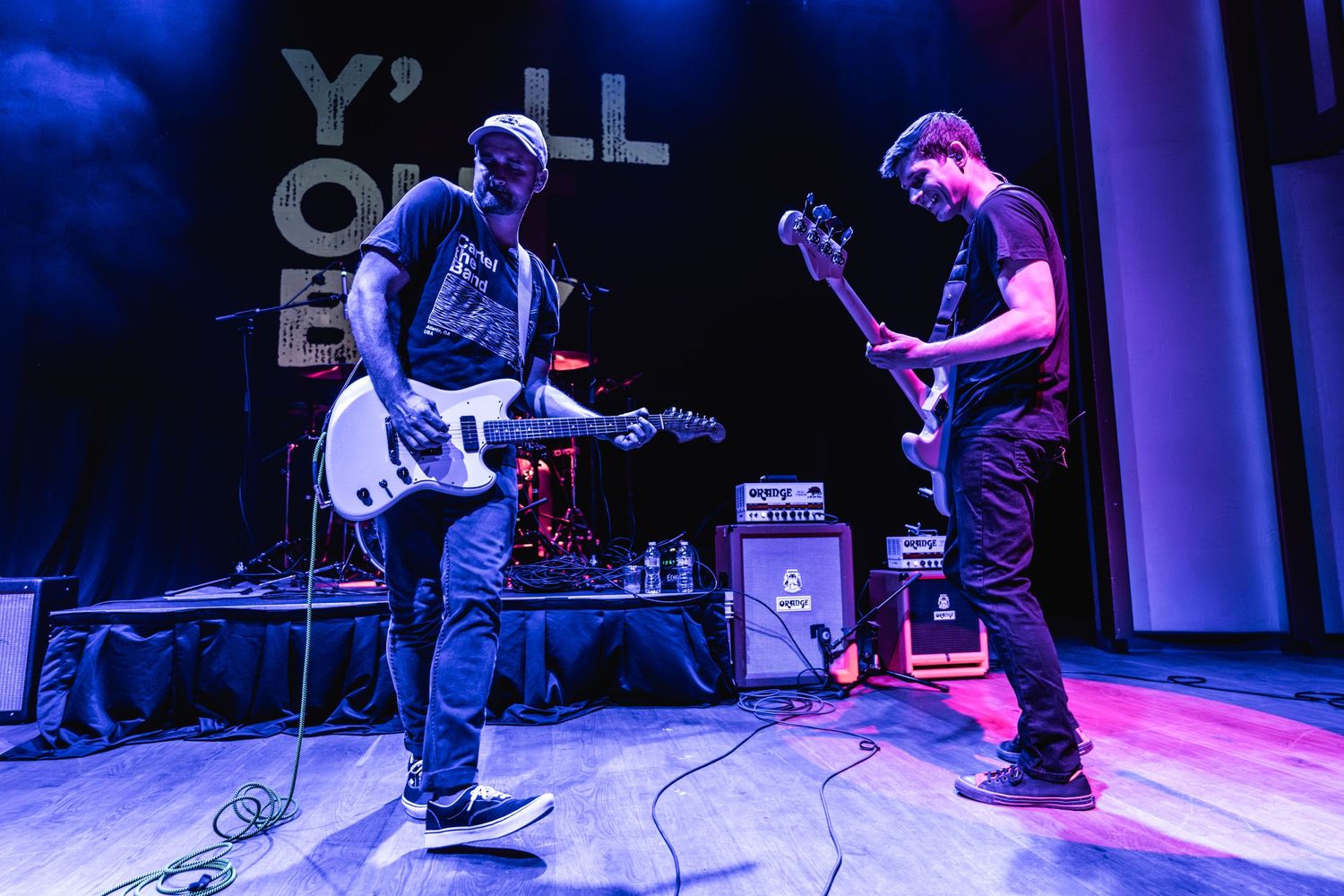 Two guitarists perform on stage with blue lighting and 'Y'all Out Boy' text visible.