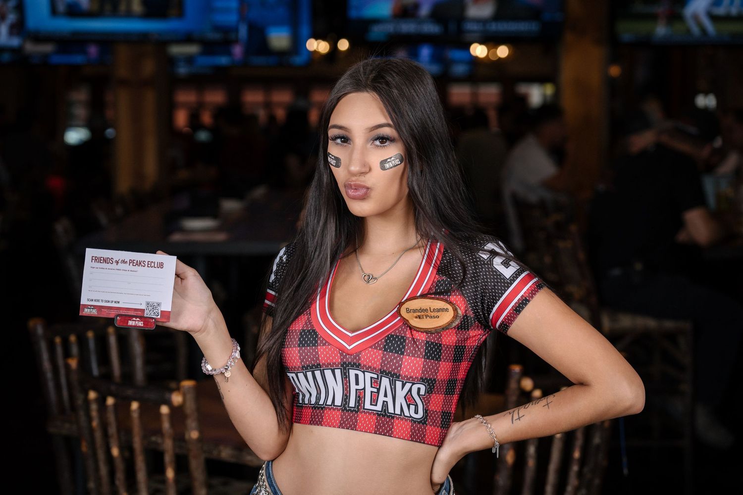 Restaurant worker displays card while modeling Twin Peaks branded uniform.