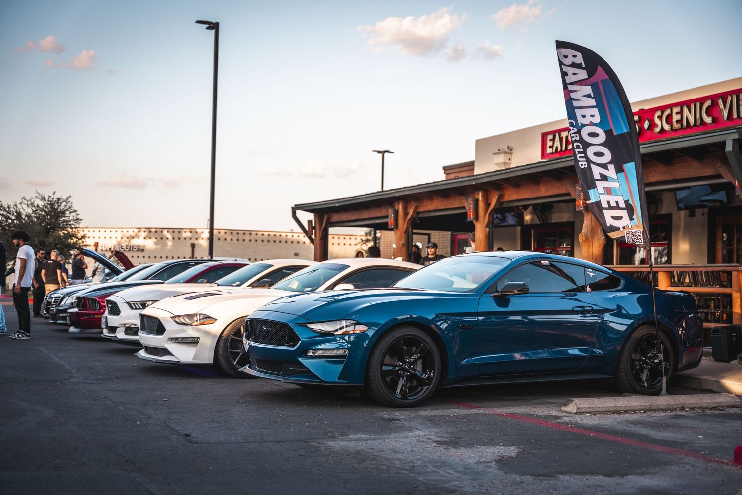 Row of modern Ford Mustangs parked outside a shopping center at sunset.