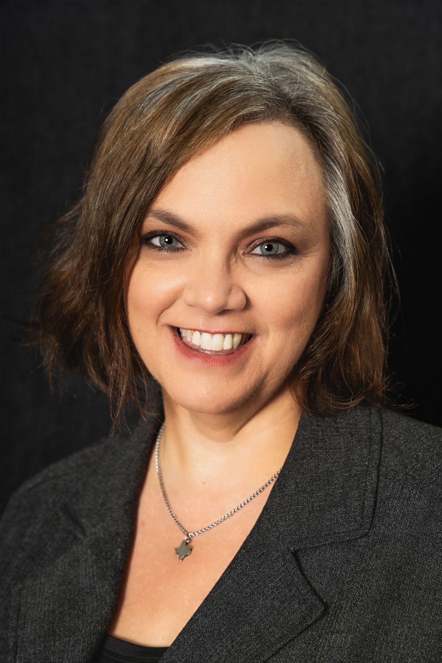 Professional studio portrait with charcoal blazer and silver jewelry against dark backdrop.