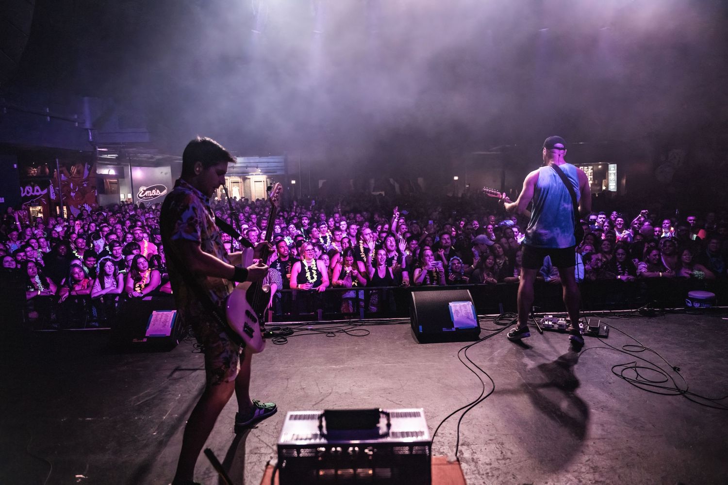 Band performs on stage to large crowd silhouetted against dramatic concert lighting.