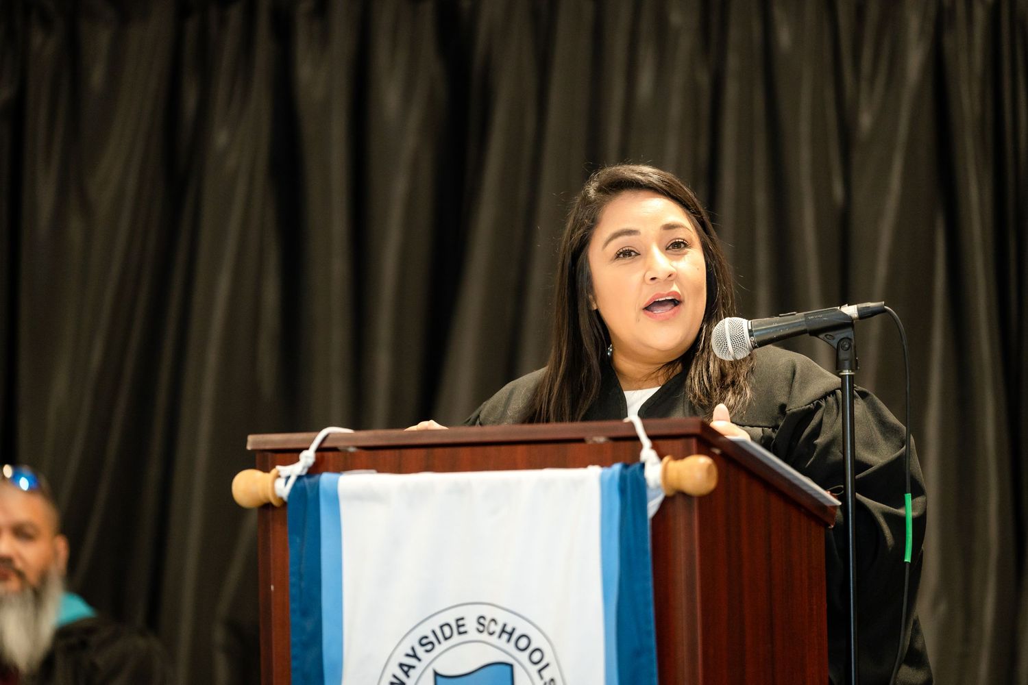 Graduate delivering commencement speech at wooden podium with university insignia.