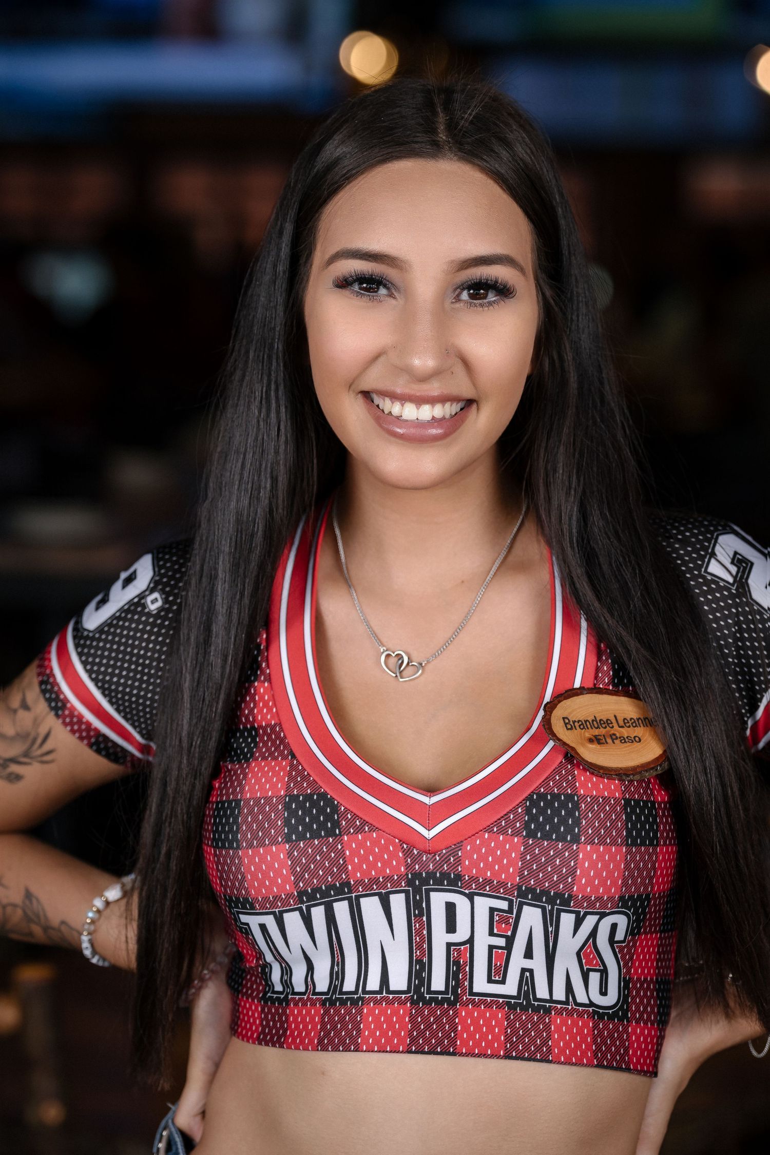 A server at Twin Peaks sports bar wearing a red and black plaid uniform top with brand logo.