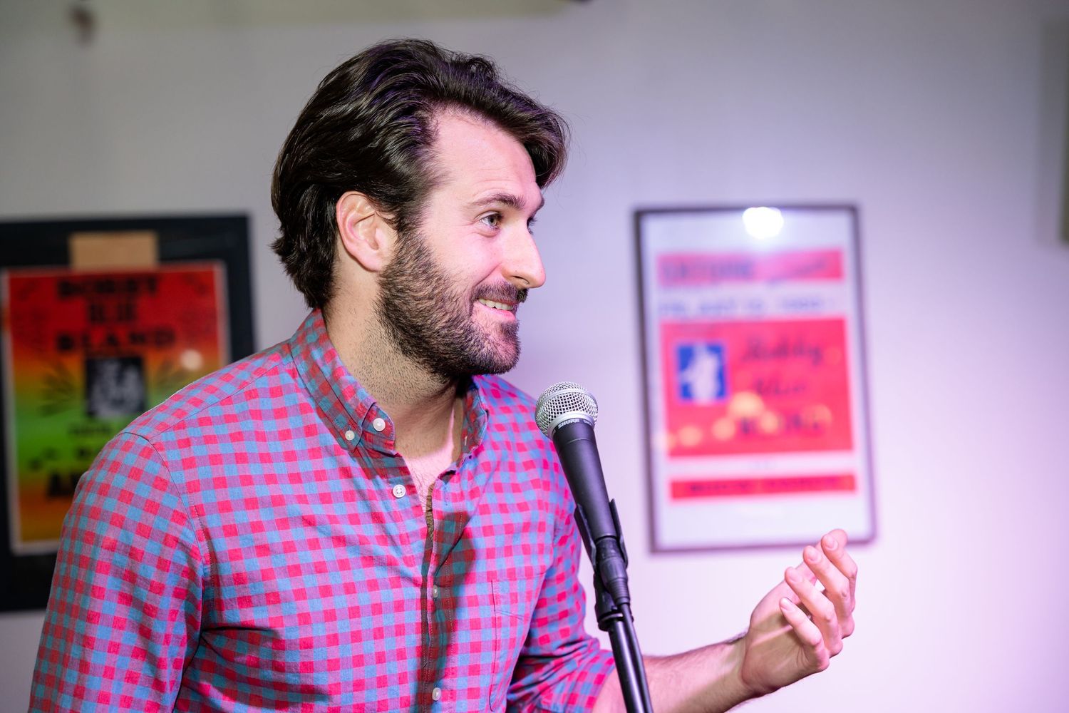 Speaker performs at a microphone against a wall with colorful art posters.