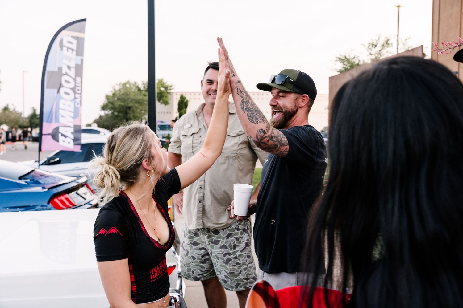 Friends celebrating and high-fiving at an outdoor car event.