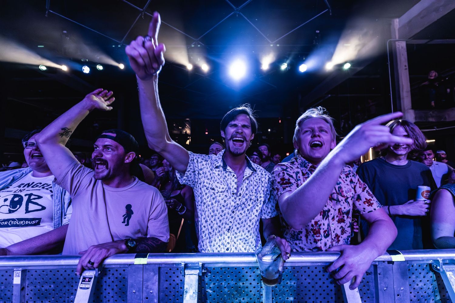 Concert crowd cheering and raising arms during high-energy performance at indoor venue.