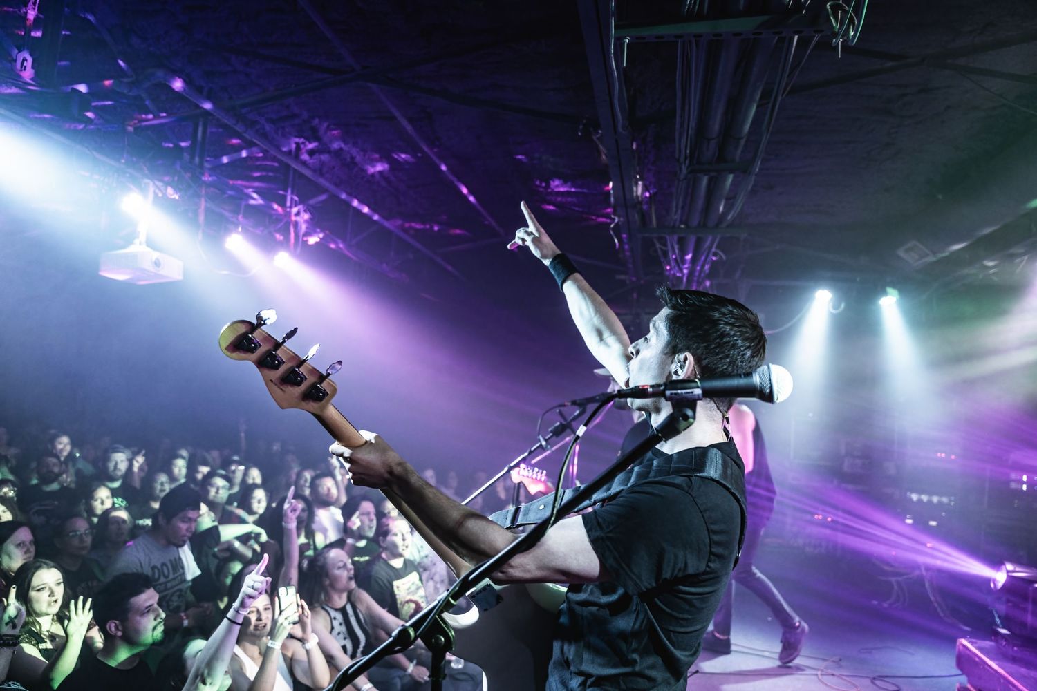 Bassist performs with dramatic stage lighting and fog effects while crowd watches from below.