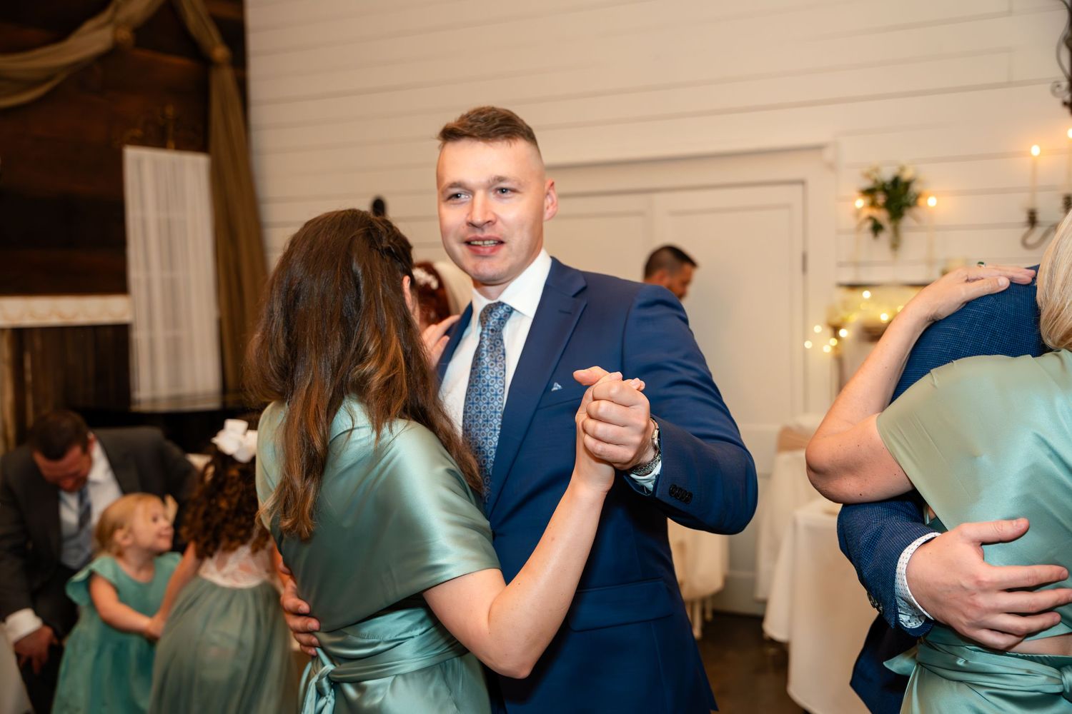 Wedding guests dancing in pairs at a reception with sage green bridesmaids' dresses.