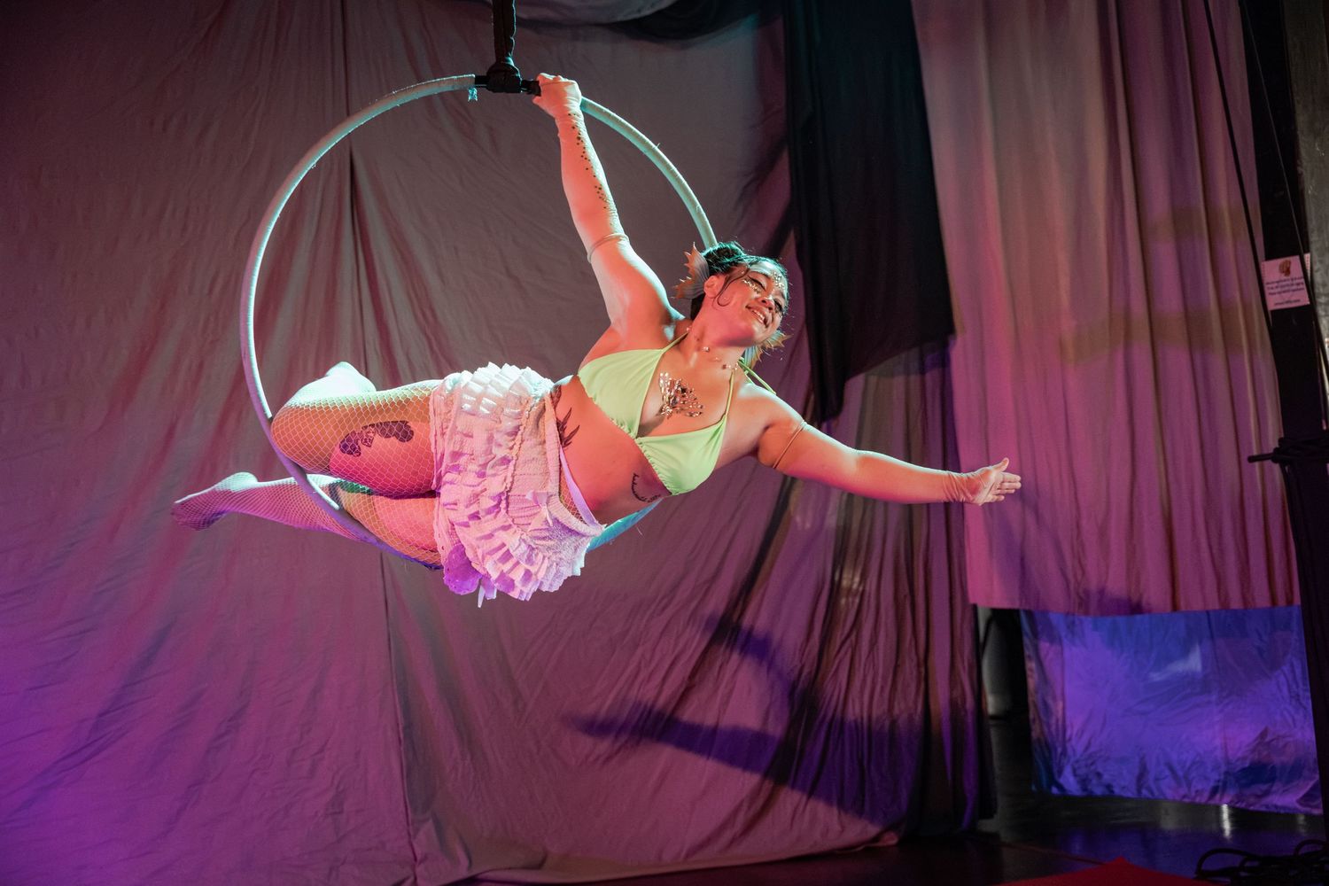Aerial hoop performer gracefully poses mid-air on a lyra ring under colorful stage lighting at a circus show.