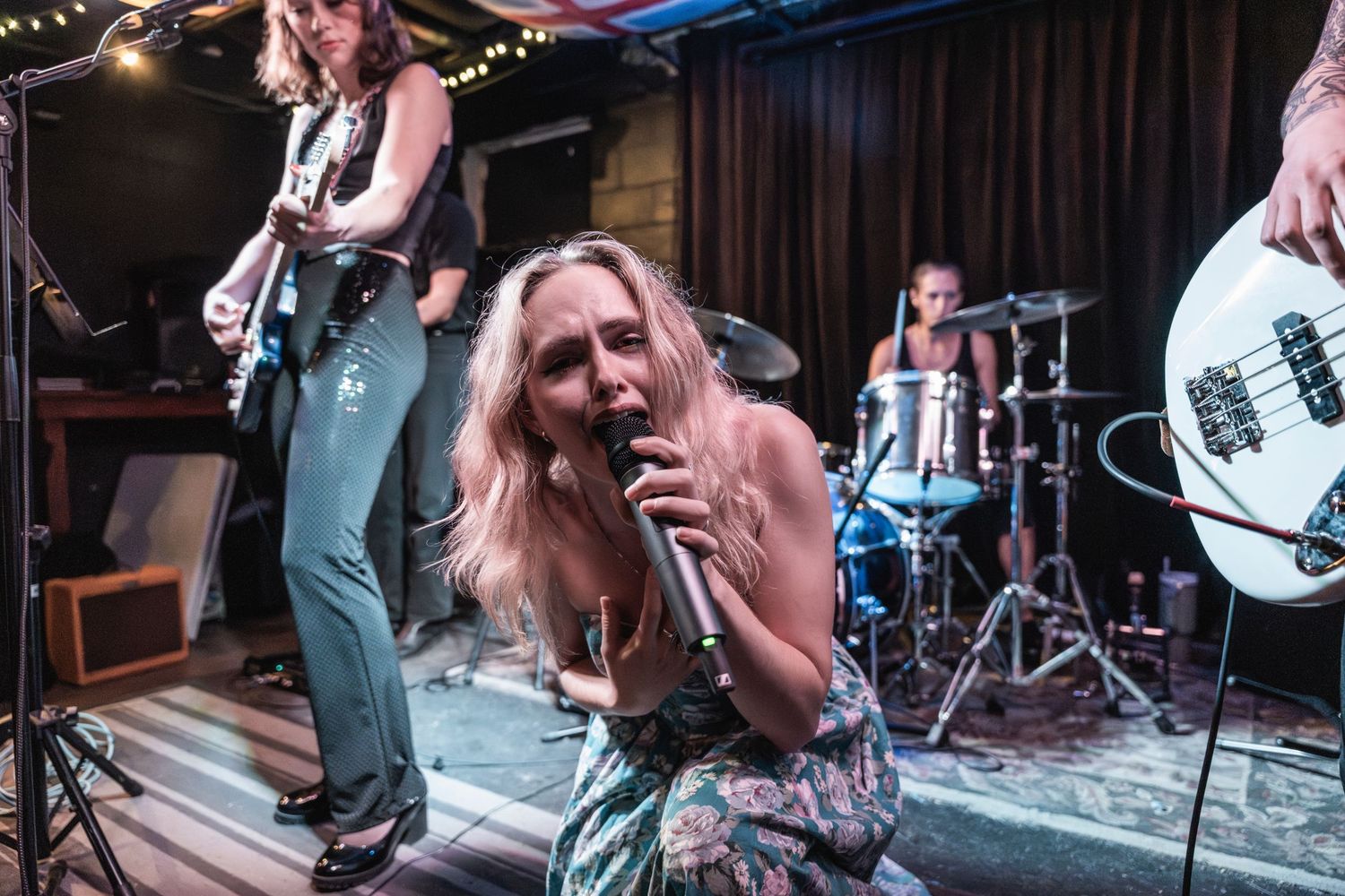 A high-energy rock band performs on stage with a vocalist and musicians playing instruments under dramatic lighting.
