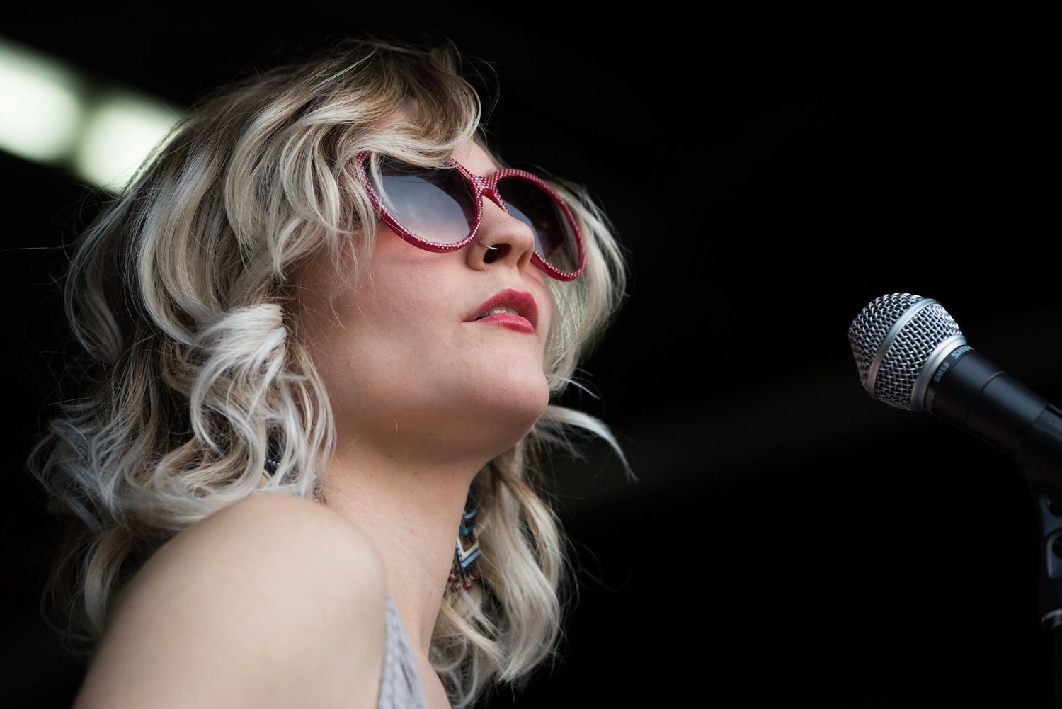 A singer with platinum blonde hair and red lipstick performs on stage with a microphone in dramatic lighting.