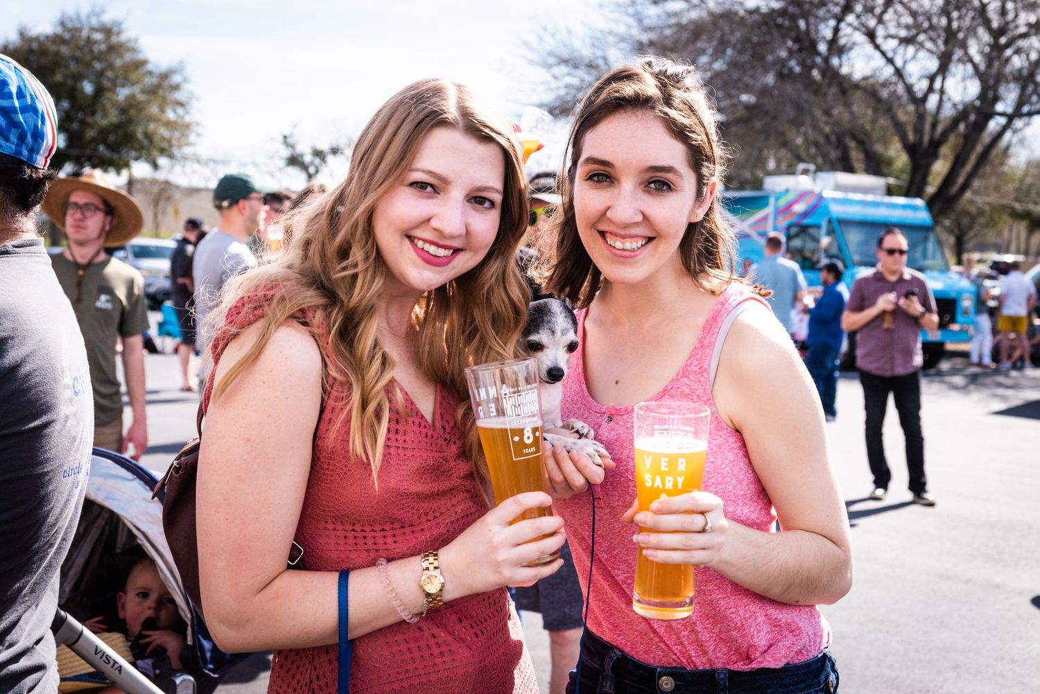 Two friends enjoying beverages at an outdoor festival on a sunny afternoon.