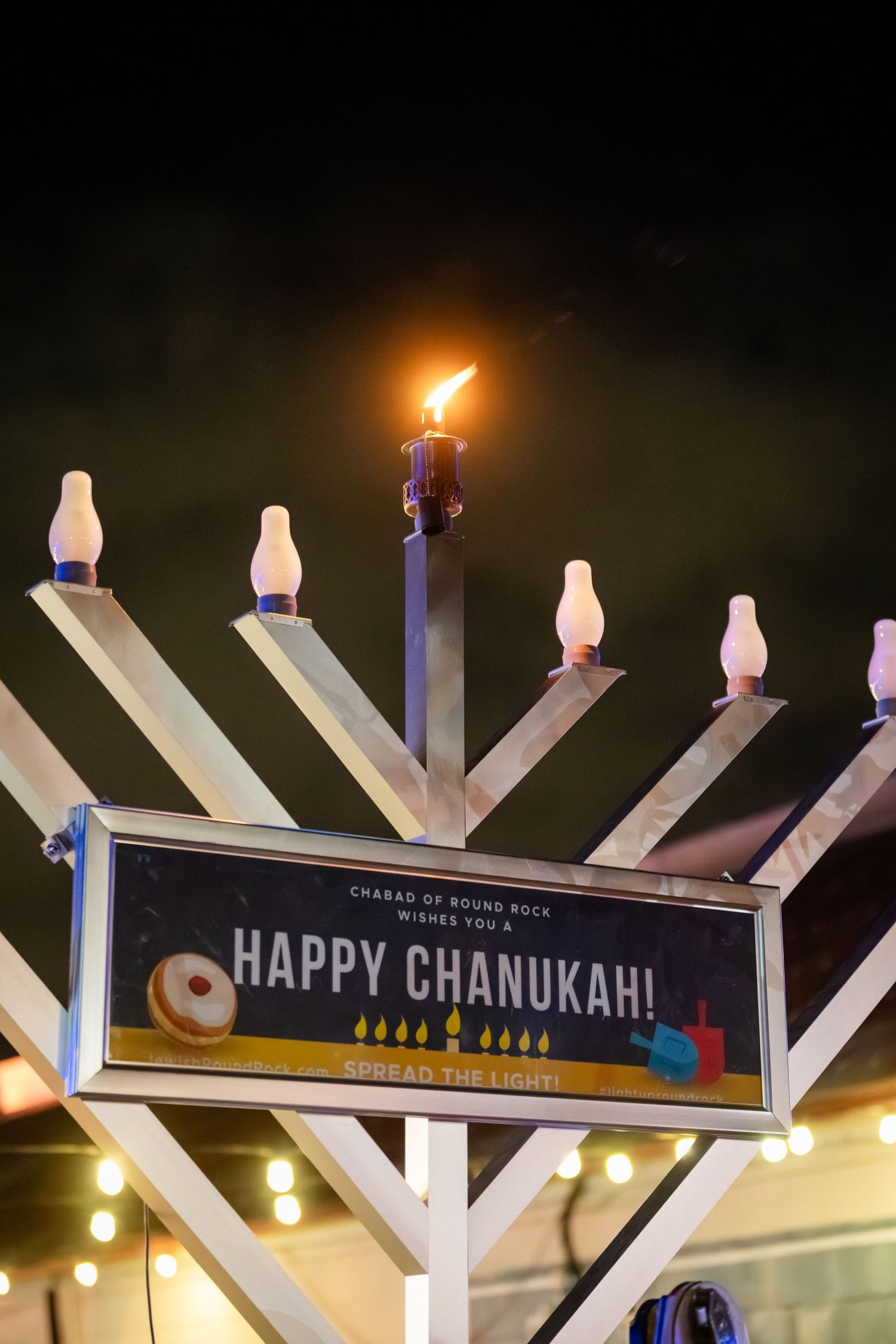 A Hanukkah menorah display with illuminated lights and 'Happy Chanukah' text glows warmly in the darkness.