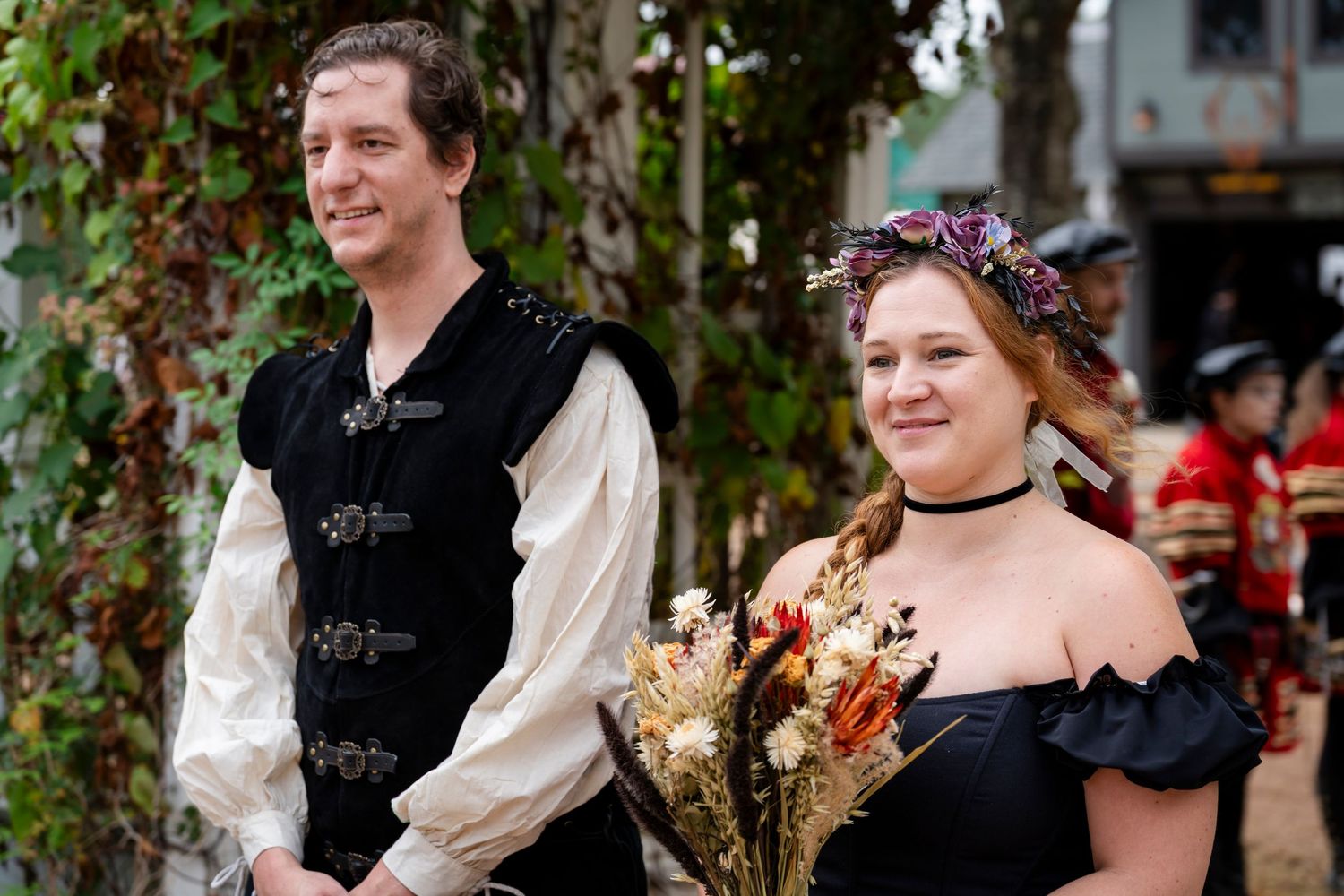A couple in Renaissance period costumes share a tender moment in a garden setting during a festival.