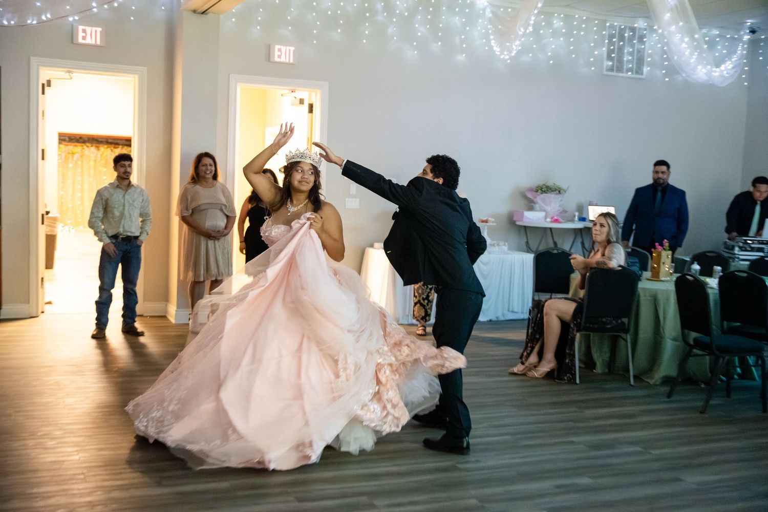 Couple shares first dance at wedding reception, bride in pink ball gown twirled by groom in elegant venue.