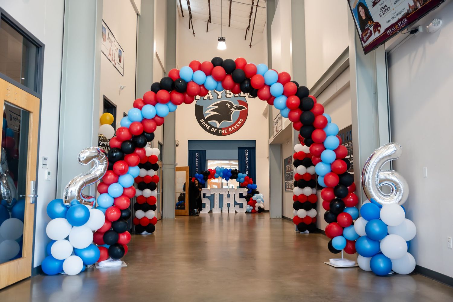 Colorful red, black, and blue balloon arch decorating a school lobby for a 5th grade celebration event.