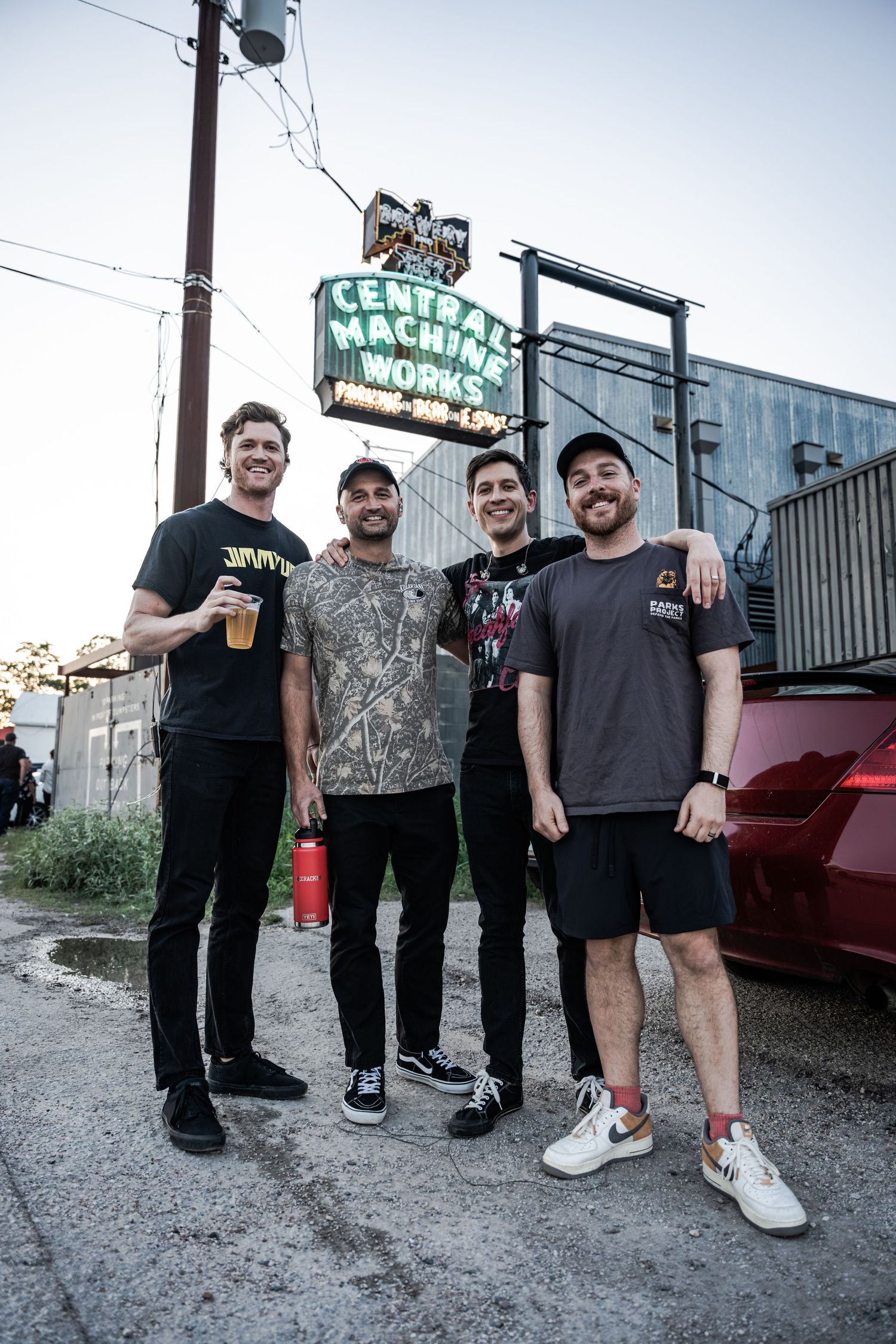 Four friends smiling together outside Central Machine Works brewery, posing for a group photo on a sunny evening.