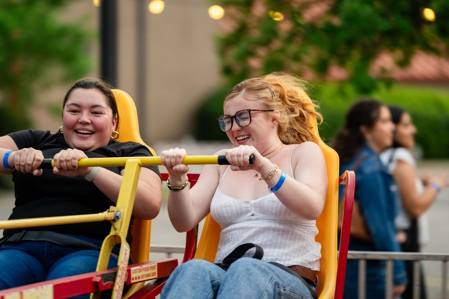 Two young women laughing and enjoying a carnival ride together at an outdoor fair event.