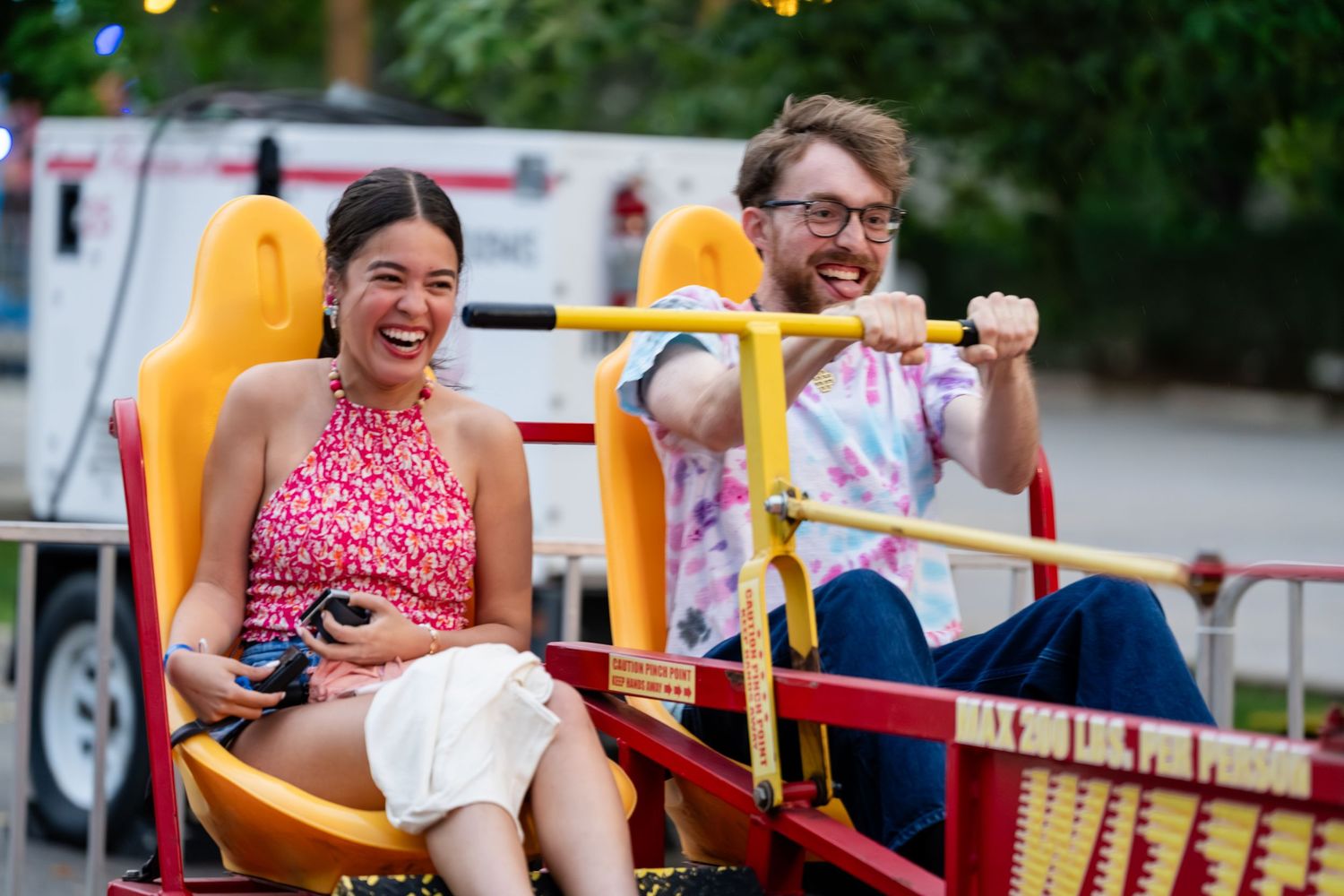 Two people laughing and enjoying a colorful amusement park ride together on a sunny day.