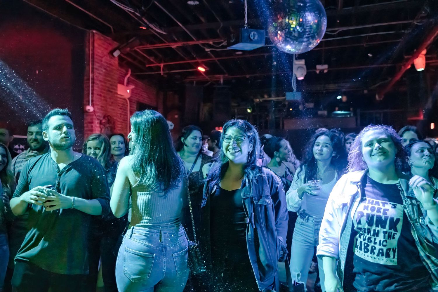 Concert crowd bathed in blue lighting watching performance beneath disco ball.