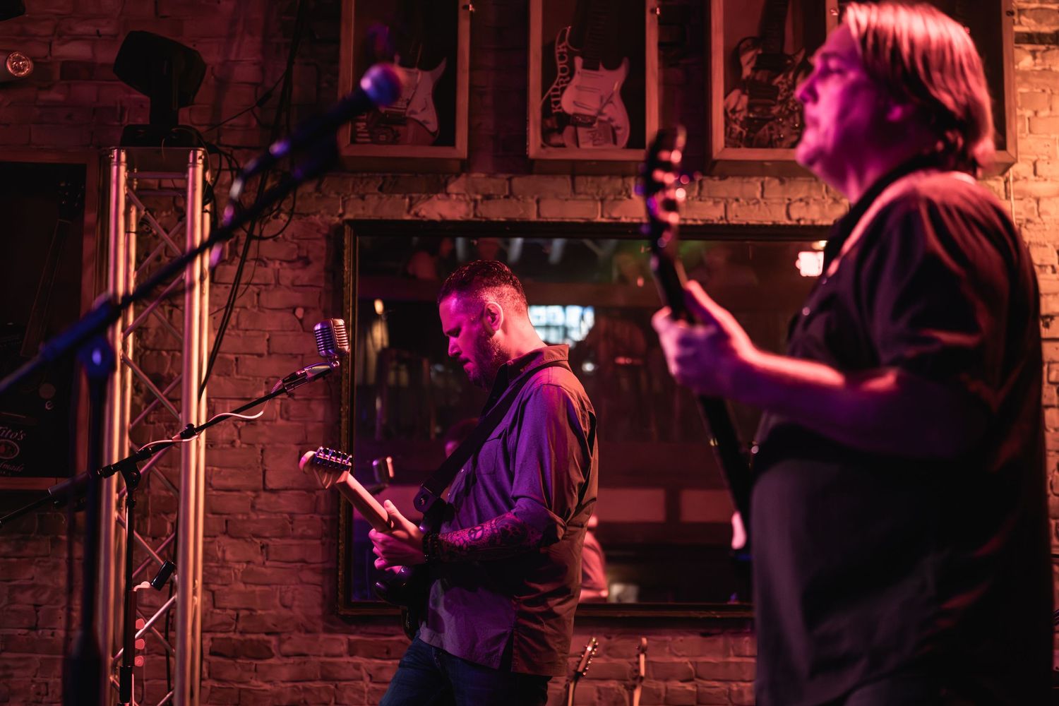 Band members perform on stage with guitars under purple lighting at an intimate venue.