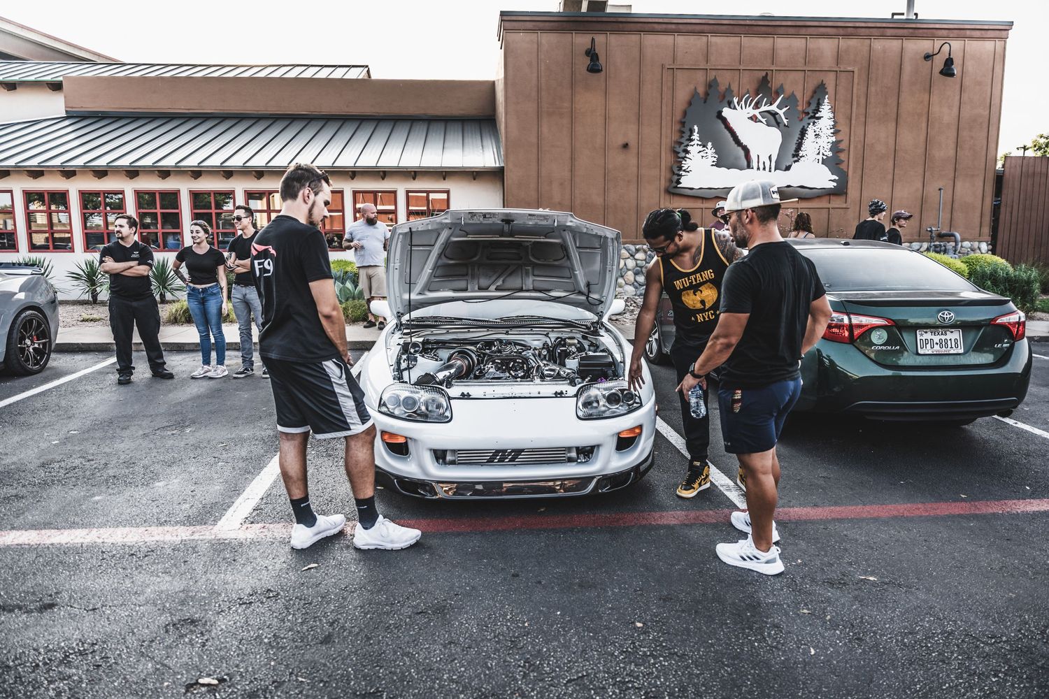 Car enthusiasts gathered around an open hood at an automotive meet.