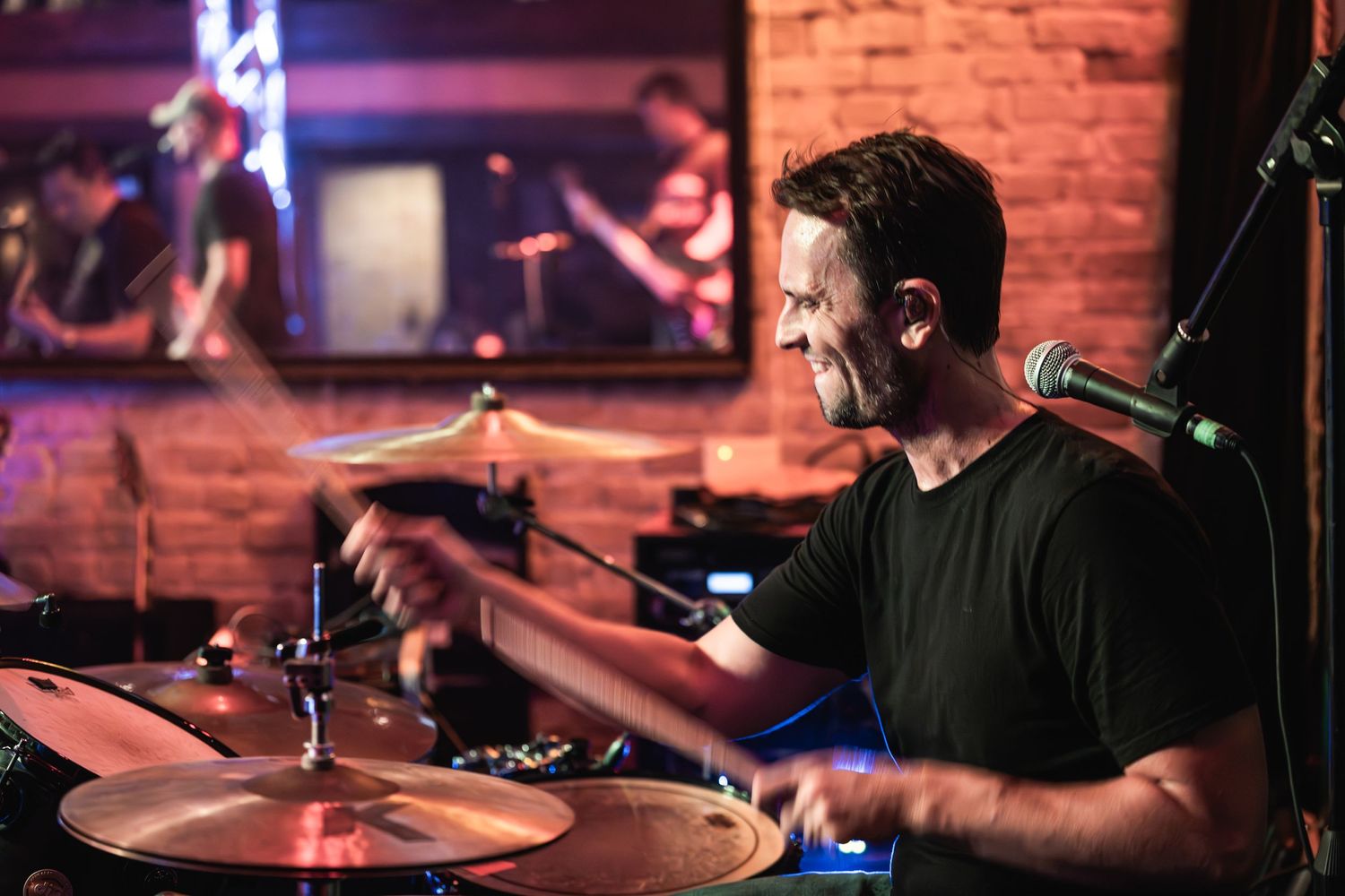 Drummer performs energetically on stage with dramatic lighting effects.
