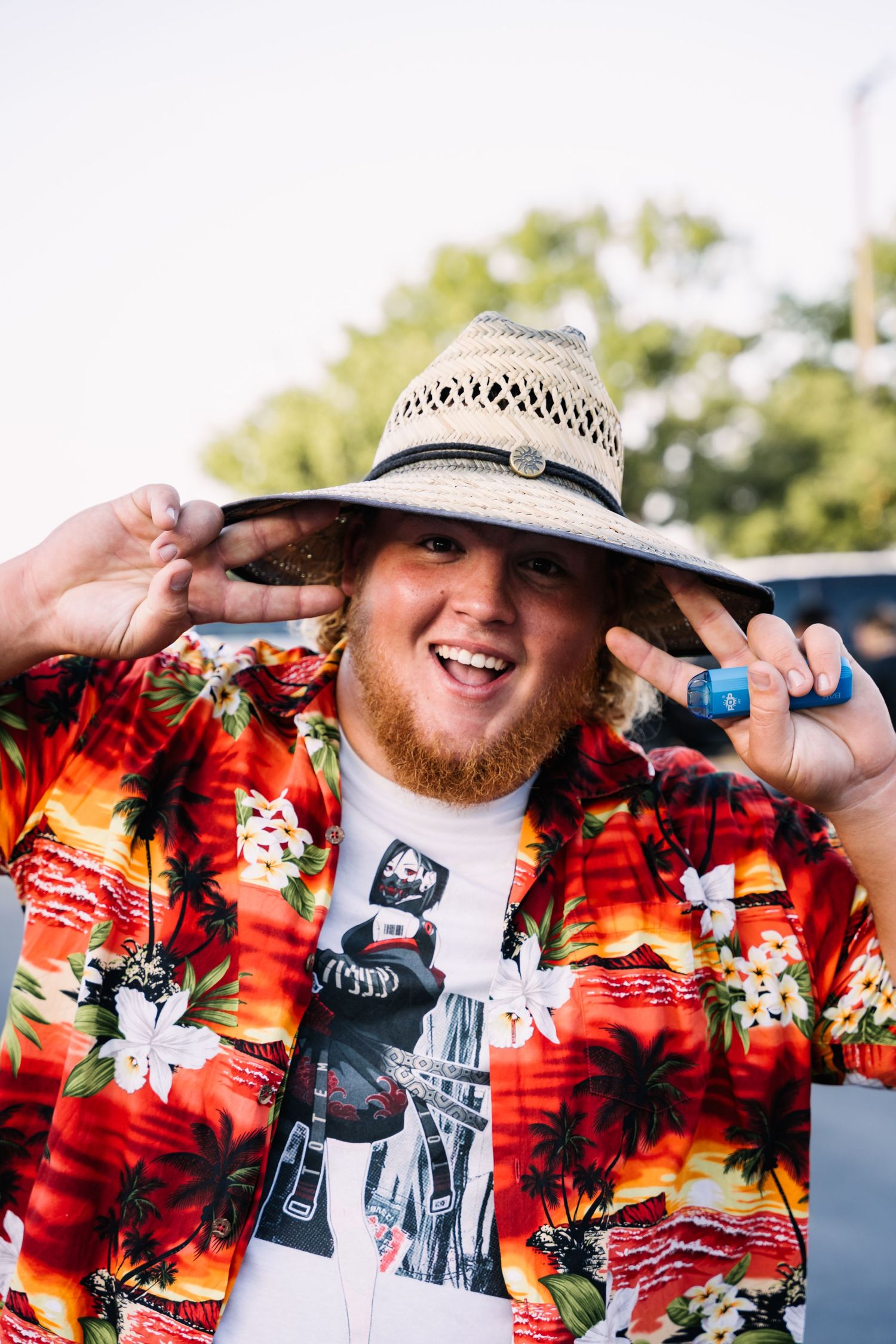 A person wearing a straw hat and tropical print shirt at a car meet.
