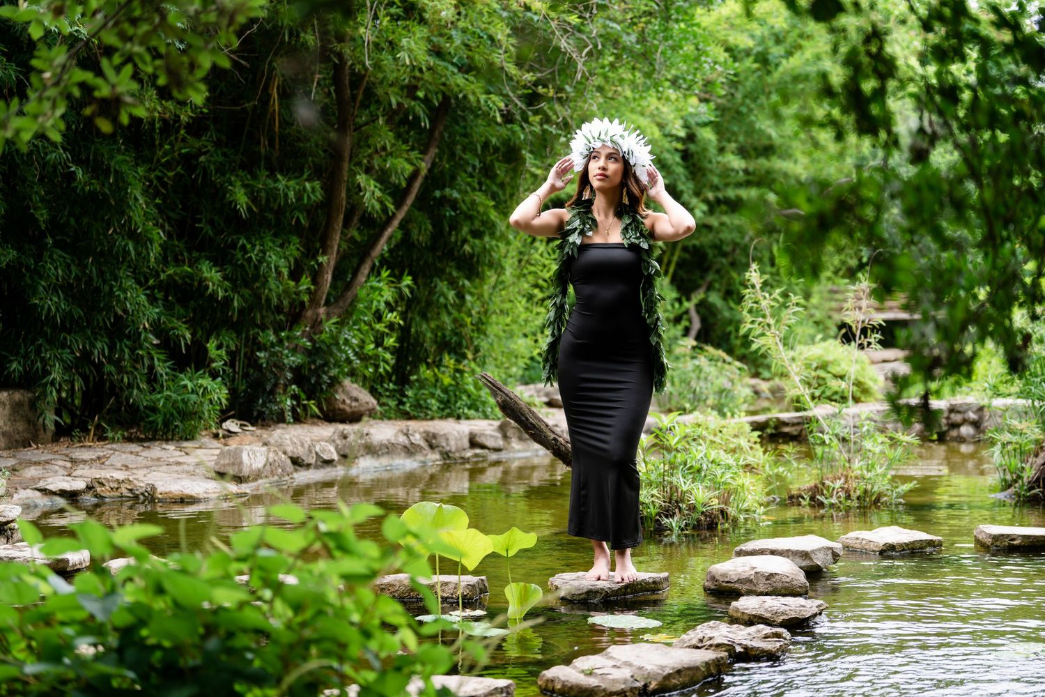 Figure in black dress walks carefully across stepping stones over serene pond.