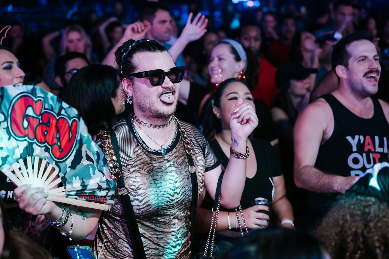 Concert-goers dance and celebrate at a music show with colorful neon lighting.
