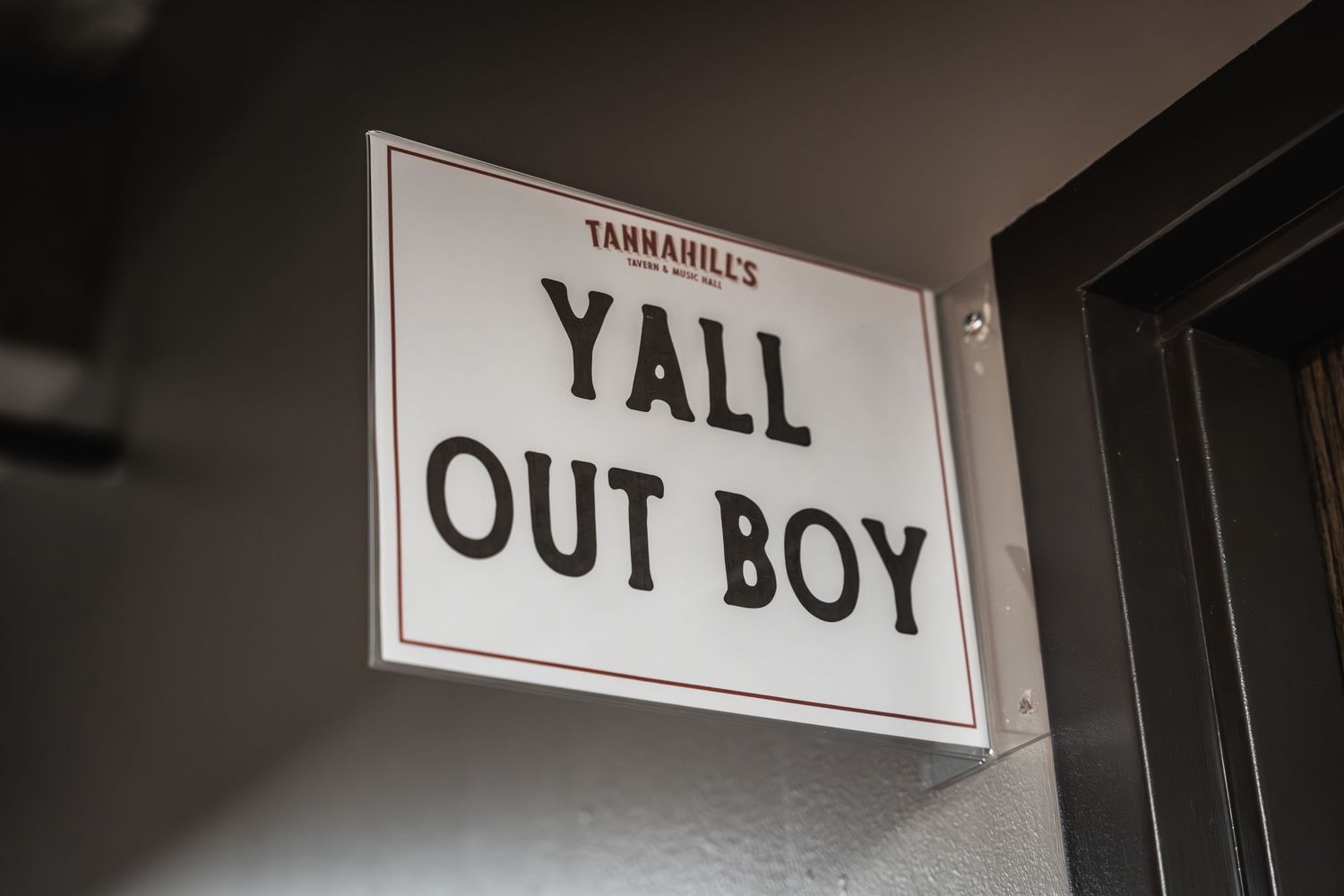 Black and white sign reading 'YALL OUT BOY' mounted on wall.