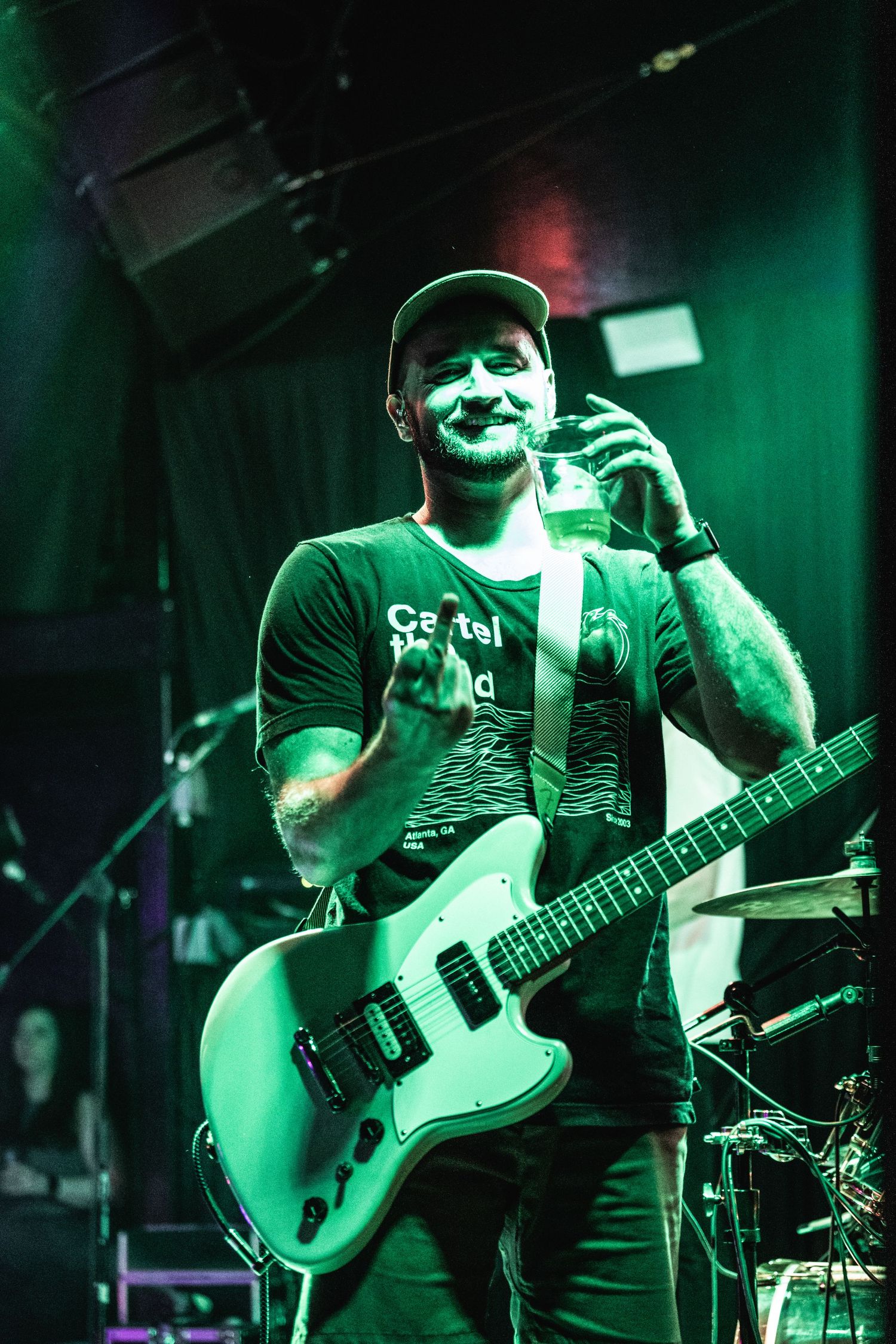 Guitarist plays electric guitar under dramatic green stage lighting.