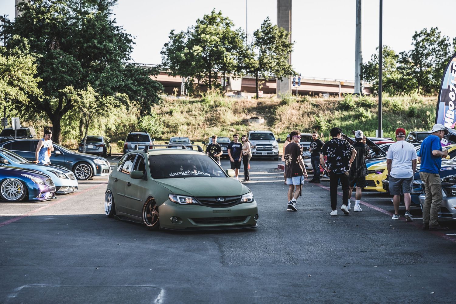 Modified green car at a car meet with people gathering in the background.