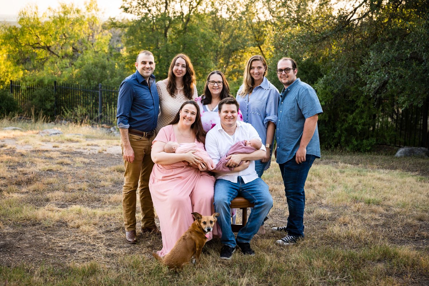 Extended family poses together outdoors with their dog at sunset.