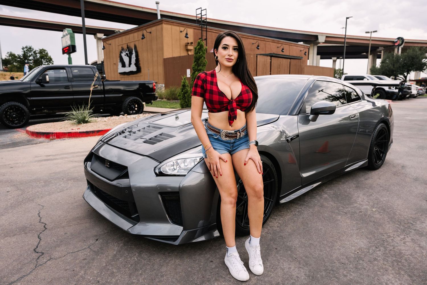 Gray Nissan GT-R sports car parked in front of urban building with red crop top and denim shorts styling.